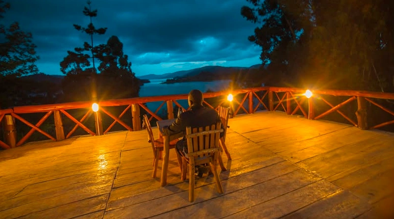 Man dining by lantern light overlooking Lake Bunyonyi at Eco Resort.