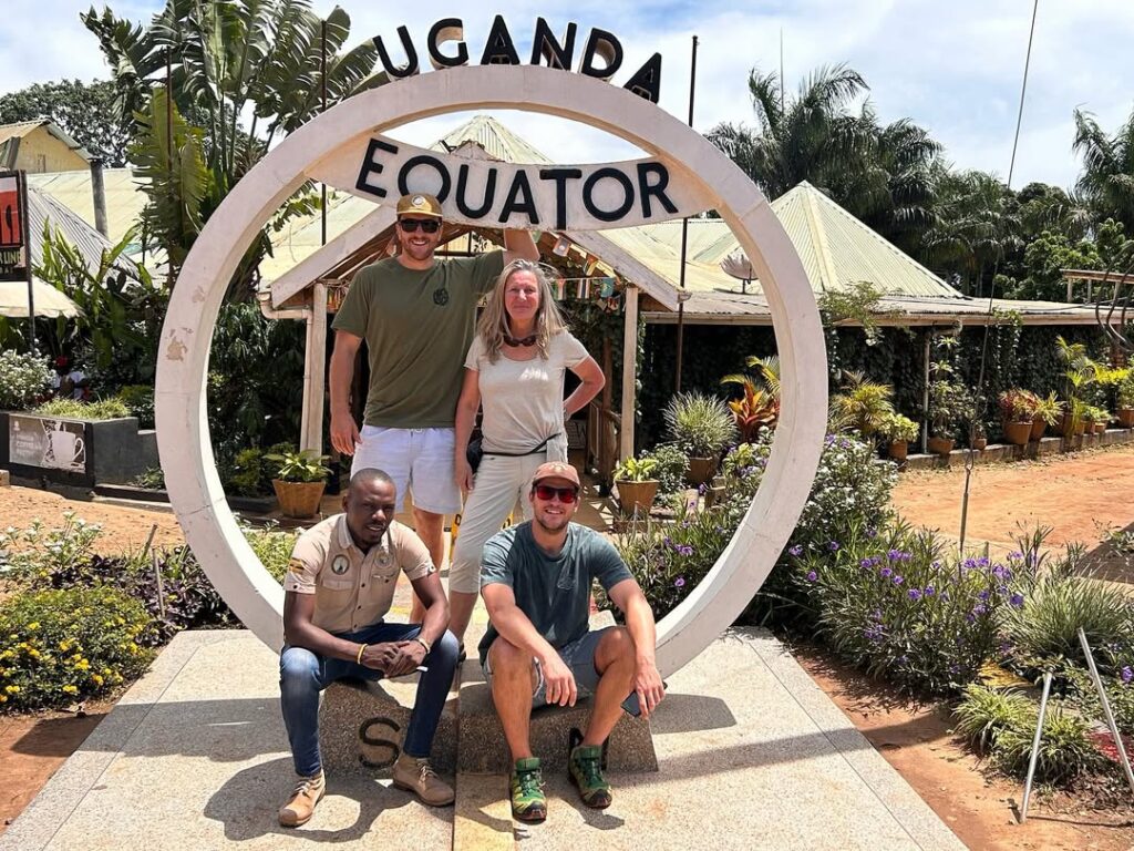 Tourists standing across the Uganda Equator line, posing between the northern and southern hemispheres with excitement and smiles