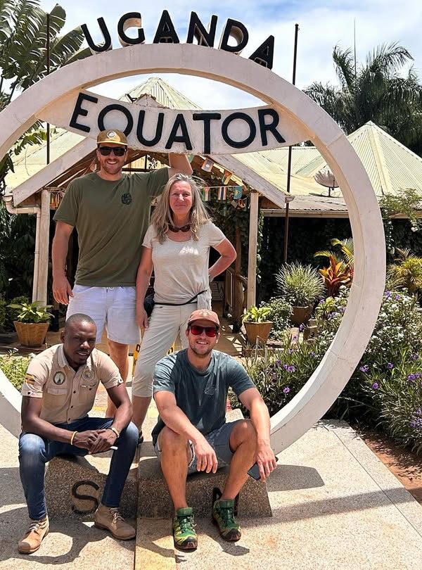 Tourists standing across the Uganda Equator line, posing between the northern and southern hemispheres with excitement and smiles