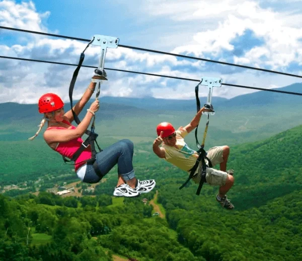 A wide, dramatic view of a couple in mid-air ziplining over the expansive Mabira Forest landscape.
