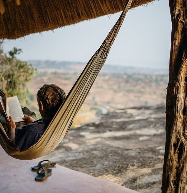 Relaxing in a hammock at Rwakobo Rock lodge, overlooking the scenic landscape of Lake Mburo National Park in Uganda. Enjoying the peaceful atmosphere and views from a private veranda.