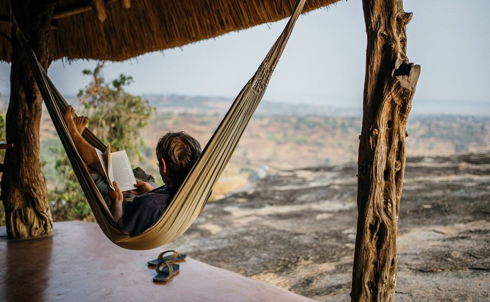 Relaxing in a hammock at Rwakobo Rock lodge, overlooking the scenic landscape of Lake Mburo National Park in Uganda. Enjoying the peaceful atmosphere and views from a private veranda.