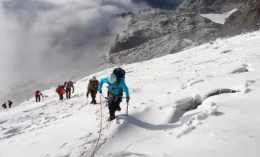 People climbing a snow-covered mountain peak in Rwenzori Mountains National Park.