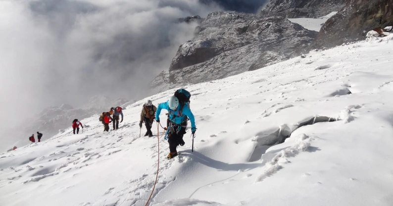 People climbing a snow-covered mountain peak in Rwenzori Mountains National Park.