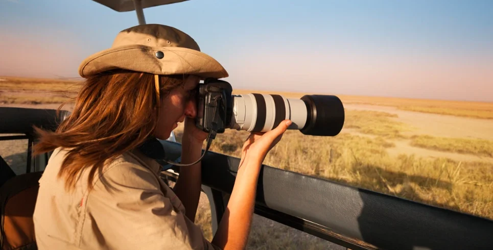 Woman photographing wildlife from safari van, highlighting gear essentials for Uganda adventures