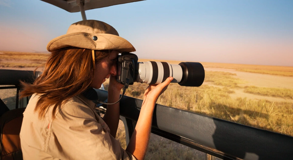 Woman photographing wildlife from safari van, highlighting gear essentials for Uganda adventures