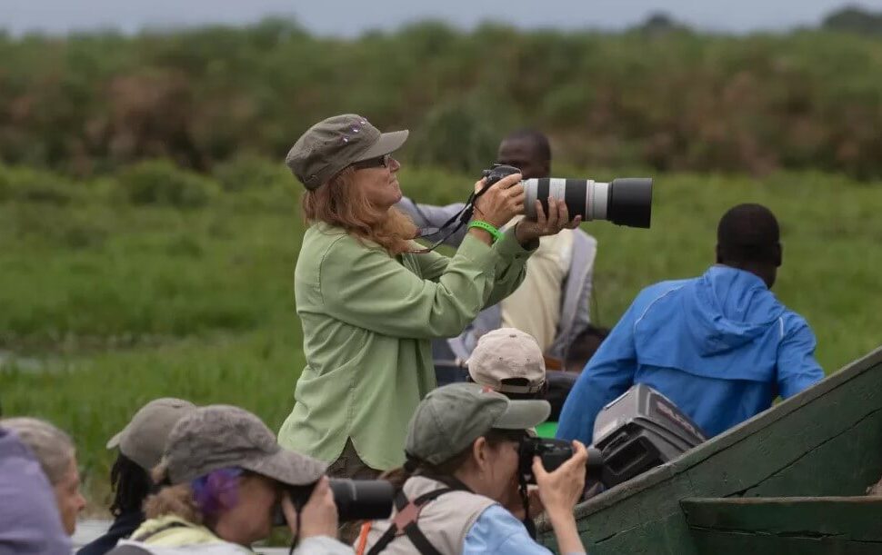 Birdwatchers in a boat on a Ugandan wetland, one person holding a large telephoto lens for bird photography