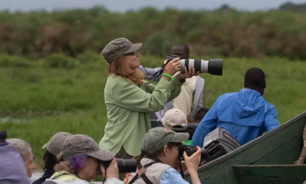 Birdwatchers in a boat on a Ugandan wetland, one person holding a large telephoto lens for bird photography