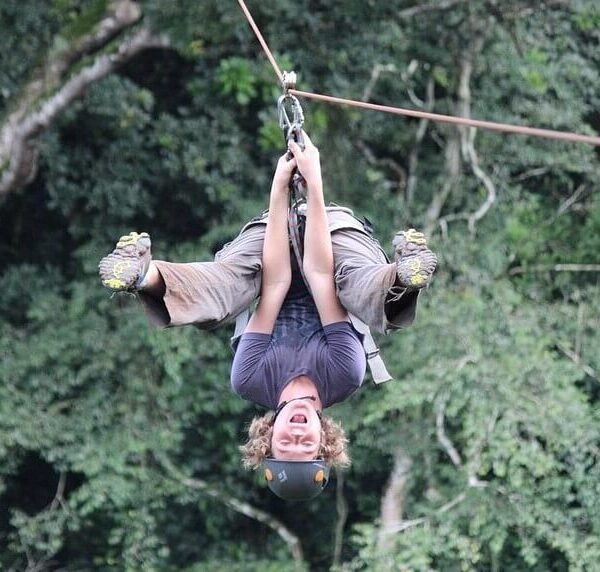 An excited tourist ziplining upside down through the green canopy of Mabira Forest in Uganda.