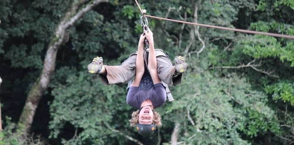 An excited tourist ziplining upside down through the green canopy of Mabira Forest in Uganda.