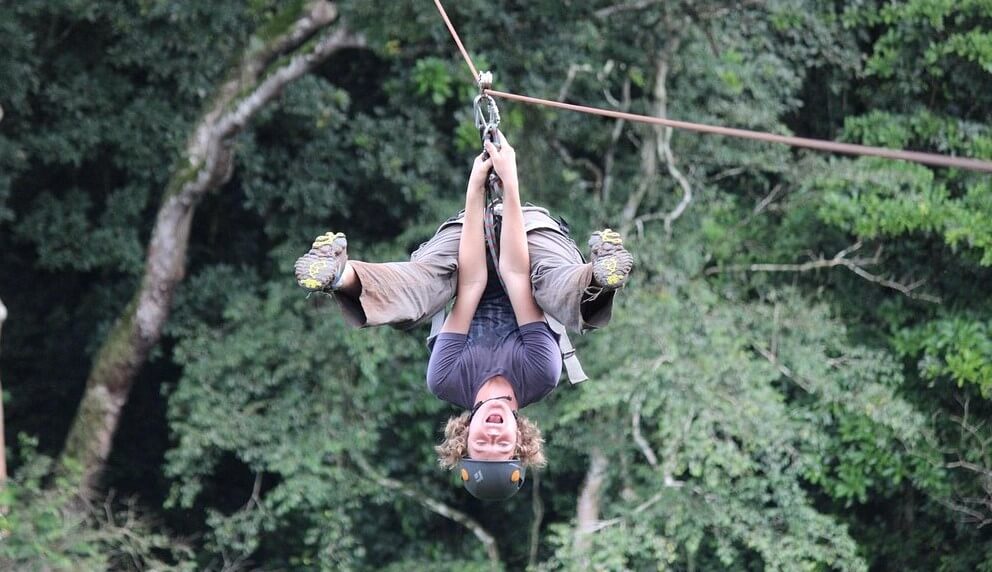 An excited tourist ziplining upside down through the green canopy of Mabira Forest in Uganda.