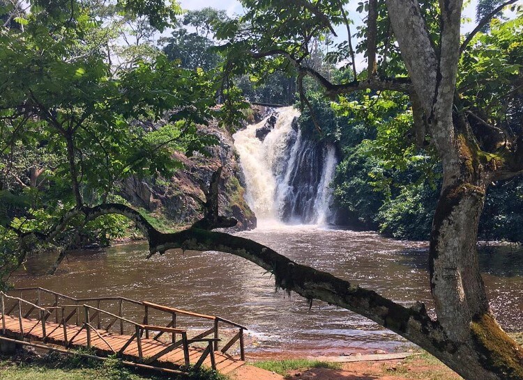 The Ssezibwa Falls flowing powerfully over rocks, viewed from across a wooden bridge in Uganda.