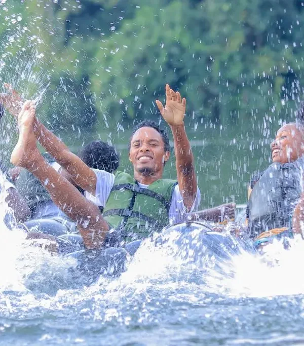 Travelers enjoying water activities and splashing in the river at Ssezibwa Falls during a day trip.