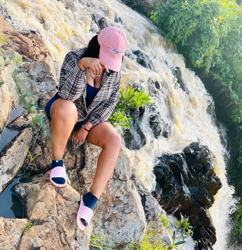 A lady sitting on the rocky top edge of Ssezibwa Falls, looking down at the cascading water in Uganda.