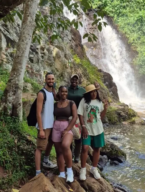 A small group of visitors standing before the cascading waters of Ssezibwa Falls, a cultural heritage site in Uganda.