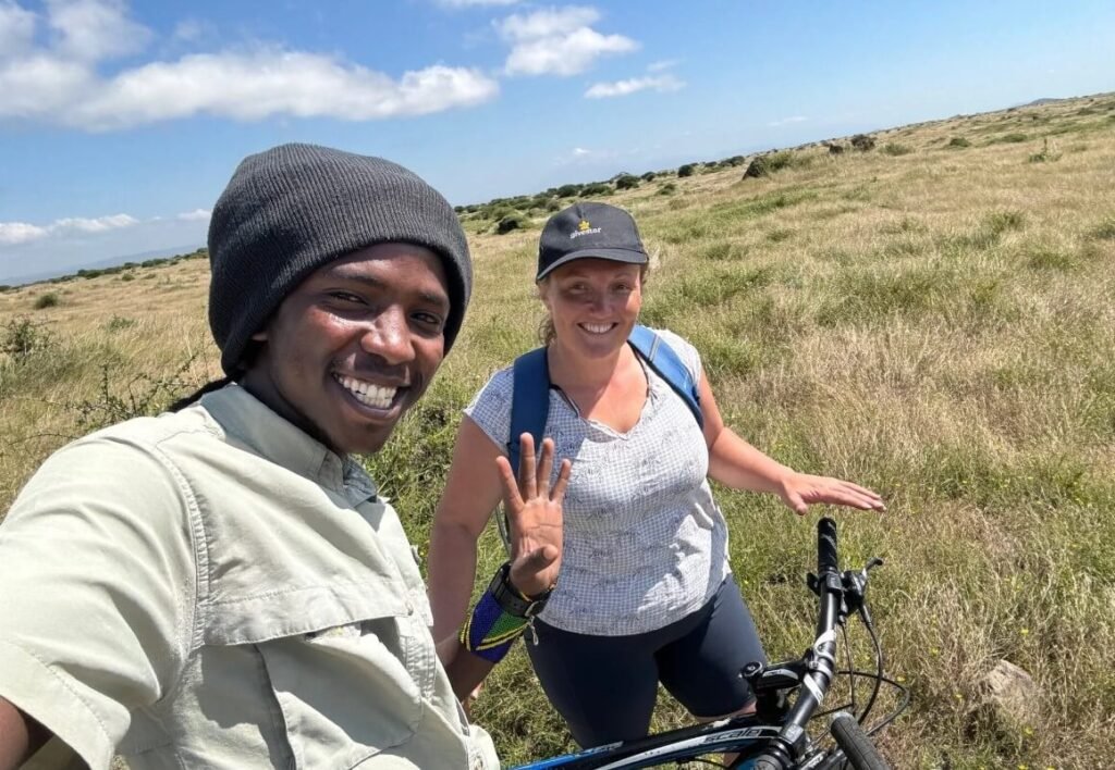 A happy solo traveler on a bicycle with their local safari guide smiling for a selfie in the savanna of Lake Mburo Safari national park