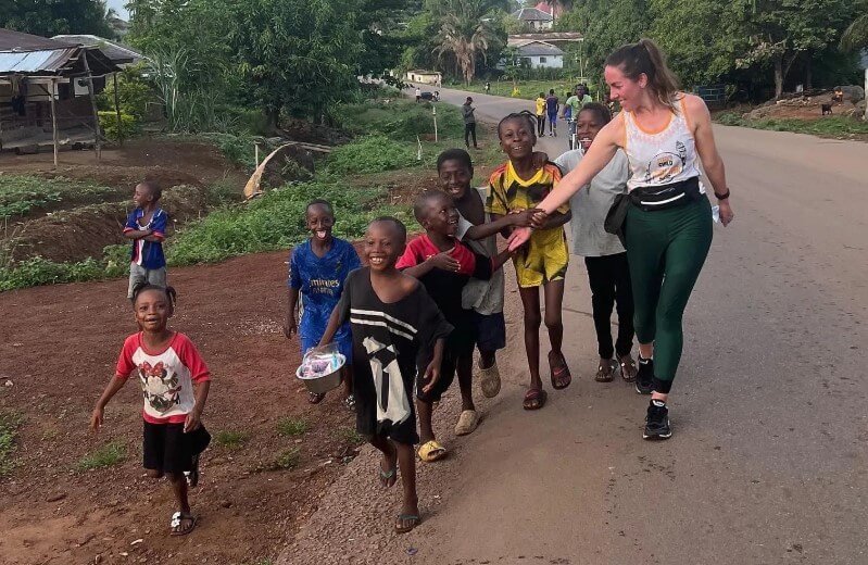 A solo traveler greeting smiling Ugandan children on a community walk near a local village, highlighting cultural immersion in Uganda.